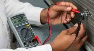 Close-up of a multimeter measuring a run capacitor on an air conditioner with red and black probes attached