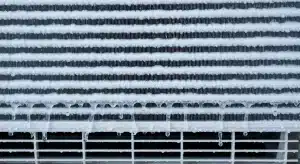 Close-up of an air conditioner evaporator coil frozen over with frost and ice dripping down